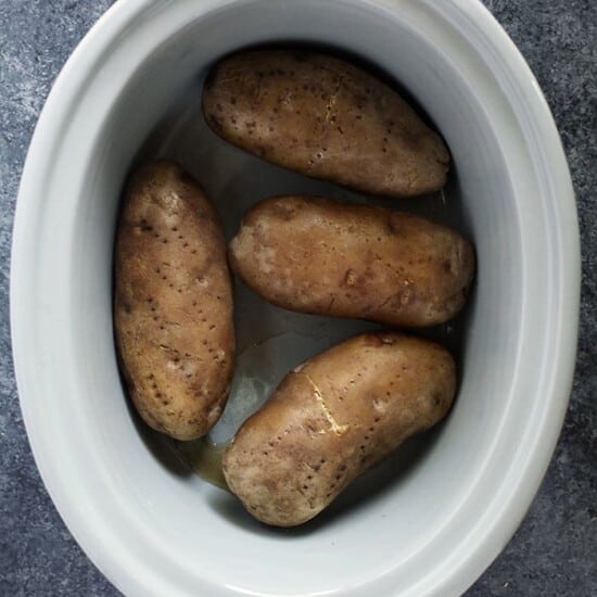 Crock pot baked potatoes served in a white bowl on a gray surface.