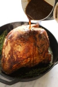 A person skillfully pours a flavorful sauce over a perfectly cooked sous vide turkey.
