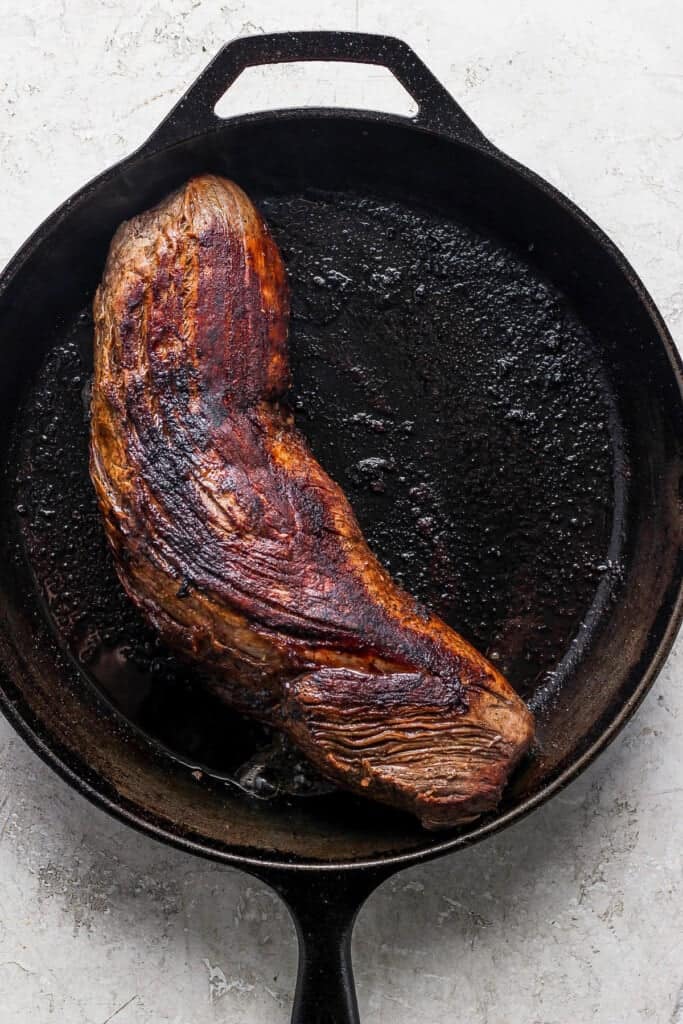A steak is being cooked in a cast iron skillet.