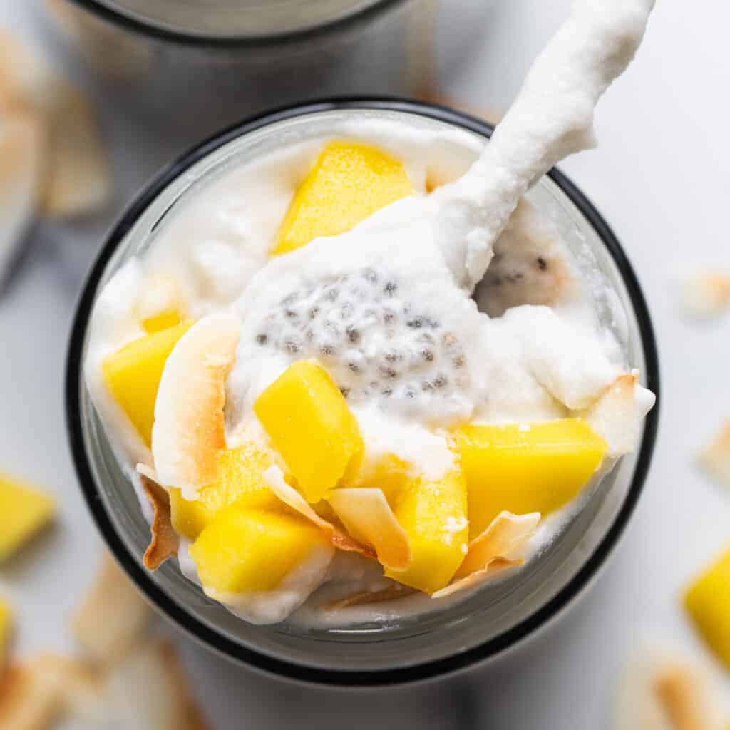 A vessel  of mango and coconut yogurt with a spoon.