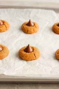 Peanut butter cookies with chocolate kisses on a baking sheet.