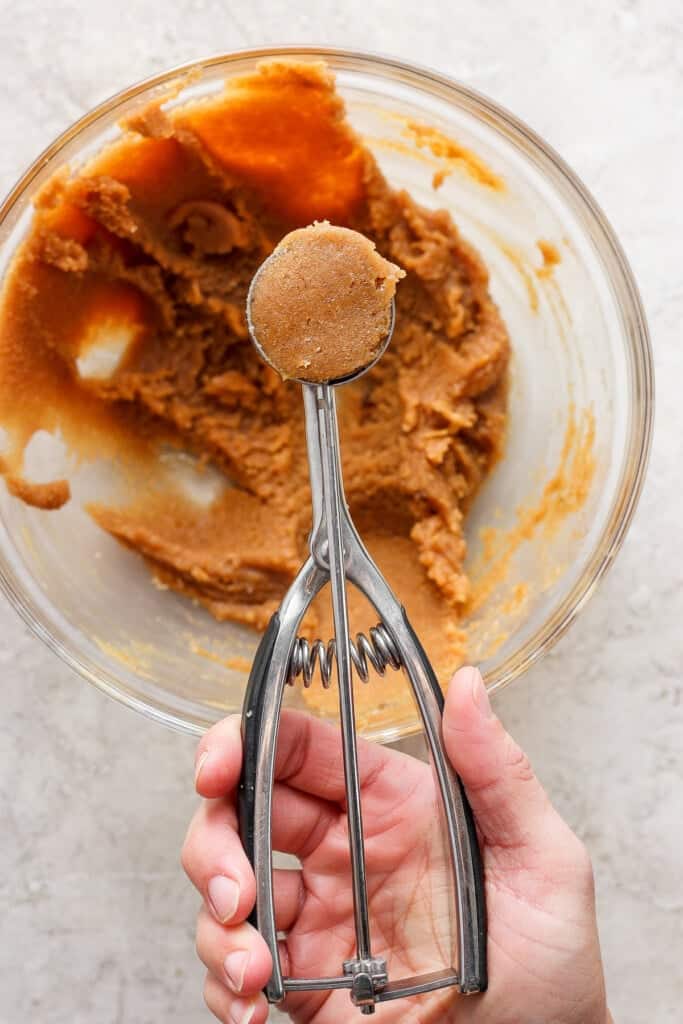 A person holding a hand mixer over a bowl of peanut butter.