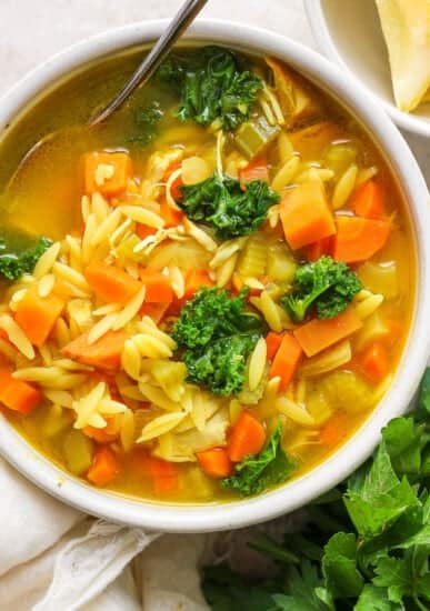 A bowl of soup with carrots and kale.