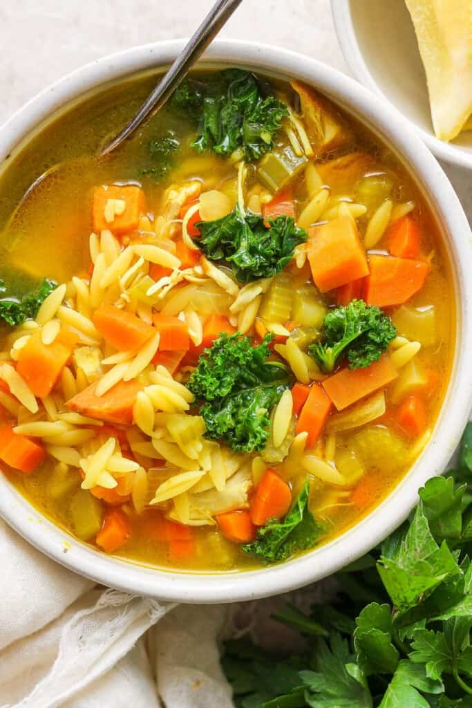 A bowl of soup with carrots and kale.