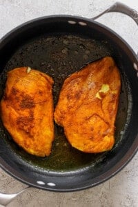 Two fried chicken breasts in a skillet.