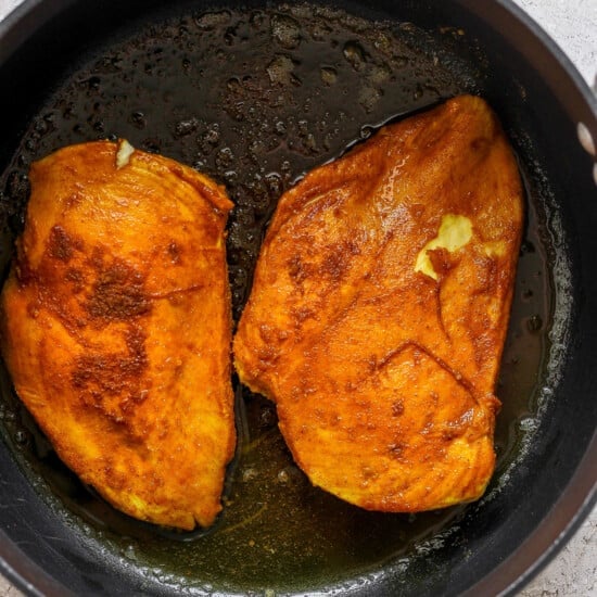 Two fried chicken breasts in a skillet.