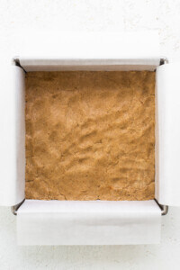 A brownie in a box on a white surface.