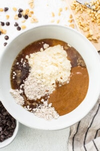 A white bowl with ingredients for a peanut butter chocolate chip cookie.