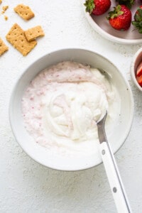 A bowl of yogurt with strawberries and crackers.