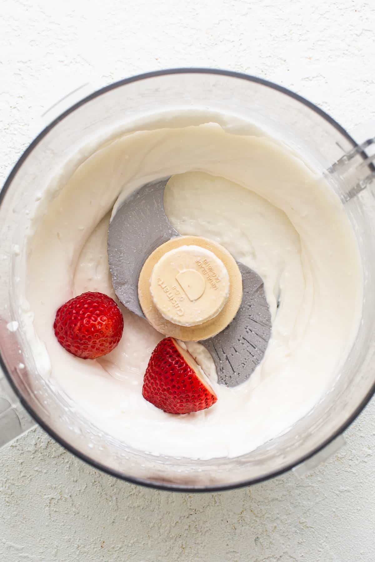 A food processor with whipped cream and strawberries.