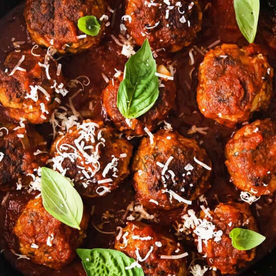 Meatballs in a skillet with basil leaves.