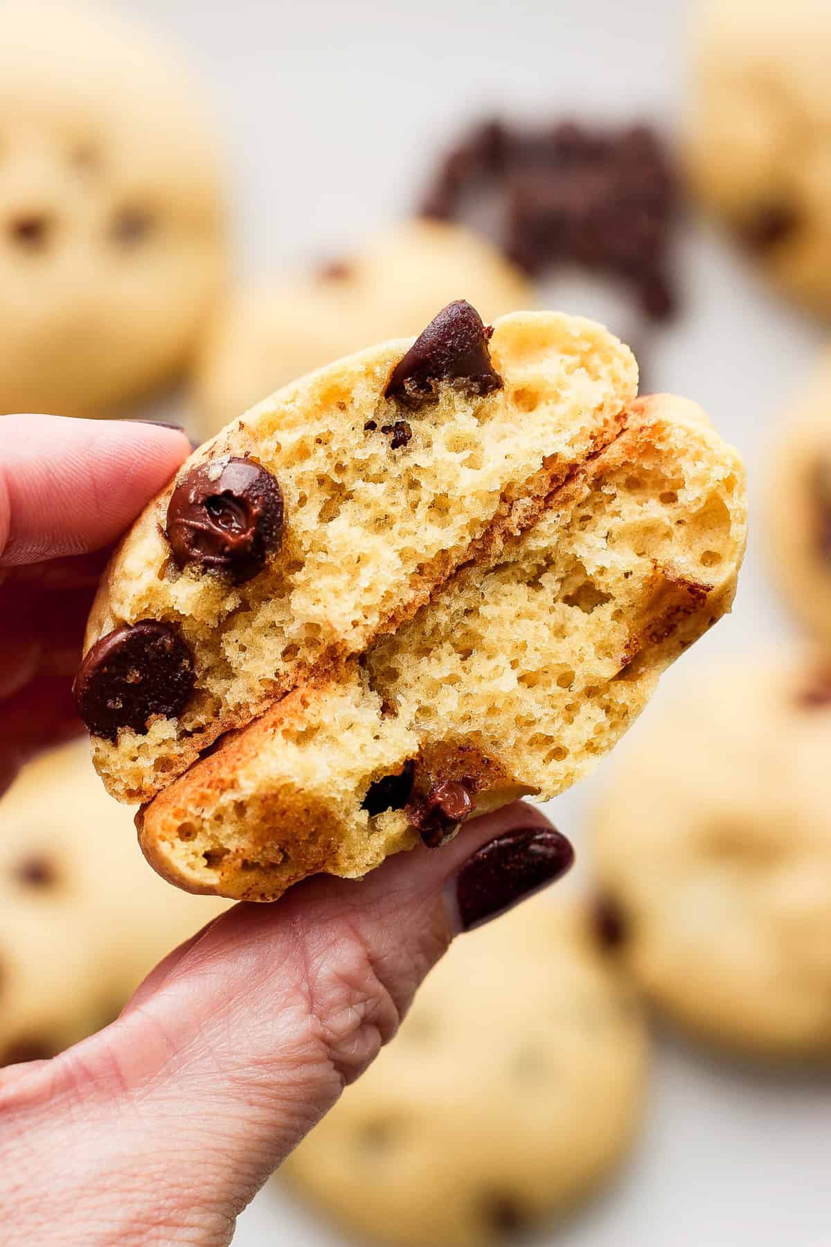 A person holding up a cookie with a bite taken out of it.