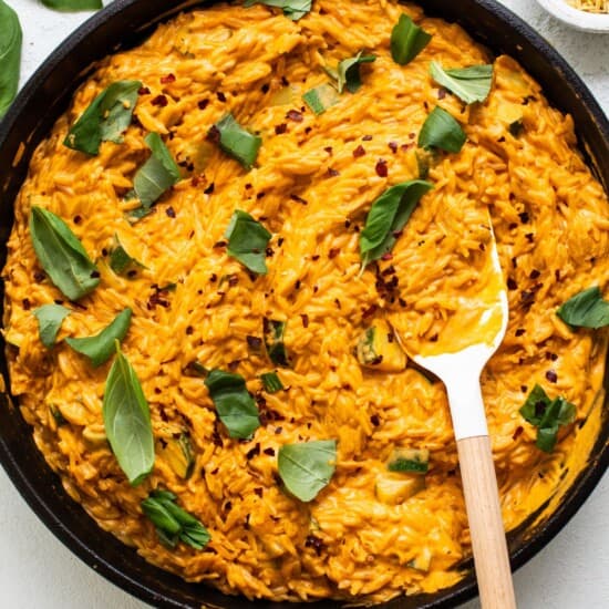 A bowl of orange risotto in a pan with a wooden spoon.