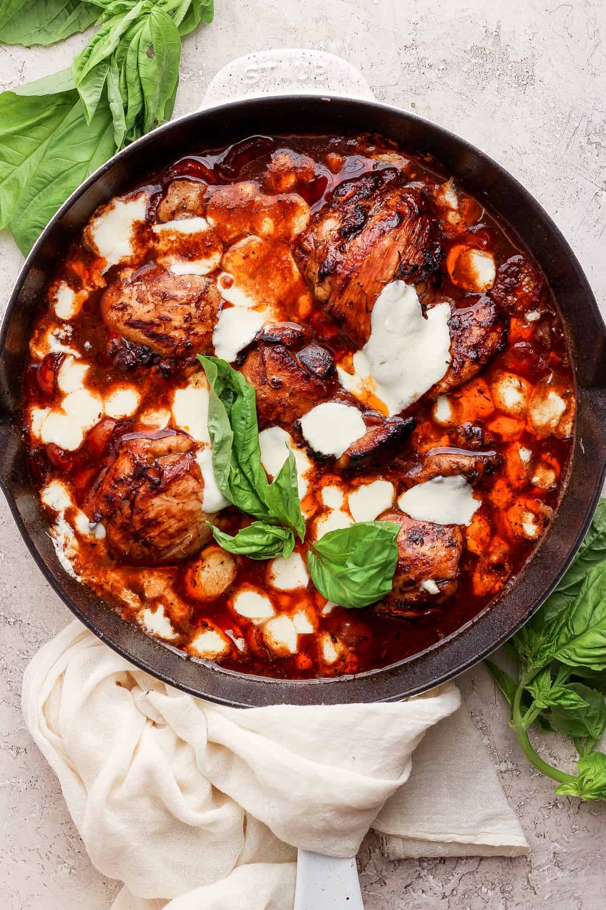 A skillet with chicken in a sauce with basil leaves.