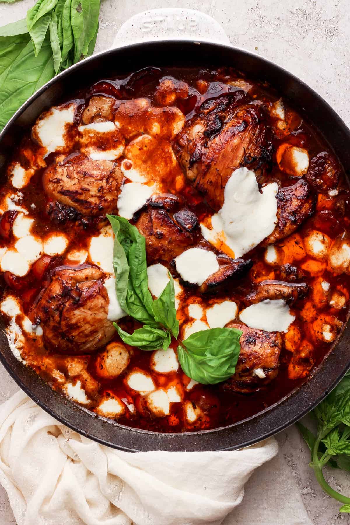 A skillet with chicken in a sauce with basil leaves.