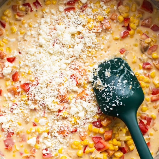 Corn chowder in a pan with a green spatula.