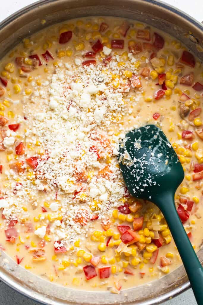 Corn in a pan with a green spatula.