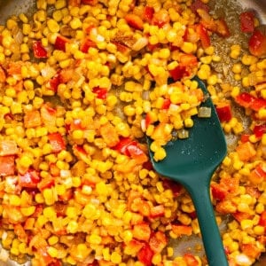 Corn in a pan with a green spatula.
