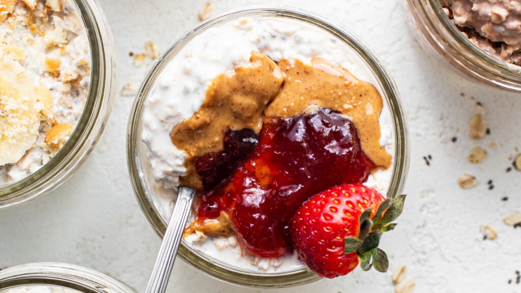 A bowl of oatmeal with peanut butter, jelly and strawberries.