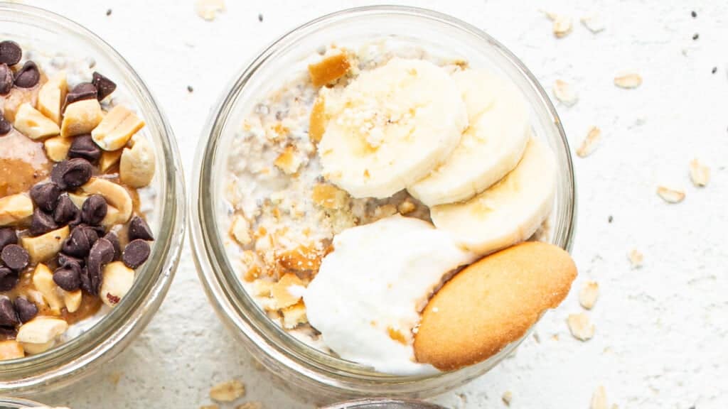 Two jars of oatmeal with bananas, nuts and whipped cream.