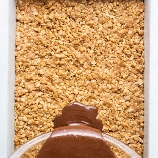 A chocolate sauce being poured over oats in a baking dish.