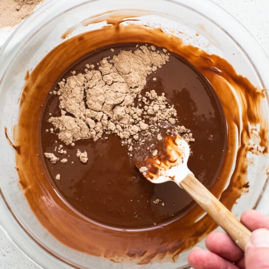 A person mixing chocolate in a bowl with a wooden spoon.
