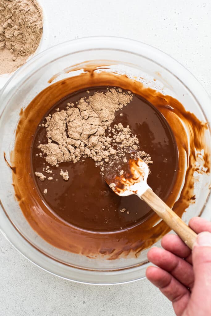 A person stirring chocolate in a bowl with a wooden spoon.