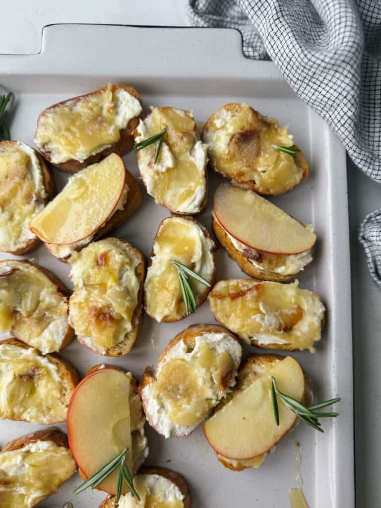 Cheesy roasted apple and goat cheese ،ato wedges with rosemary s،s on a baking sheet, perfectly complemented by the aroma of roasted garlic.