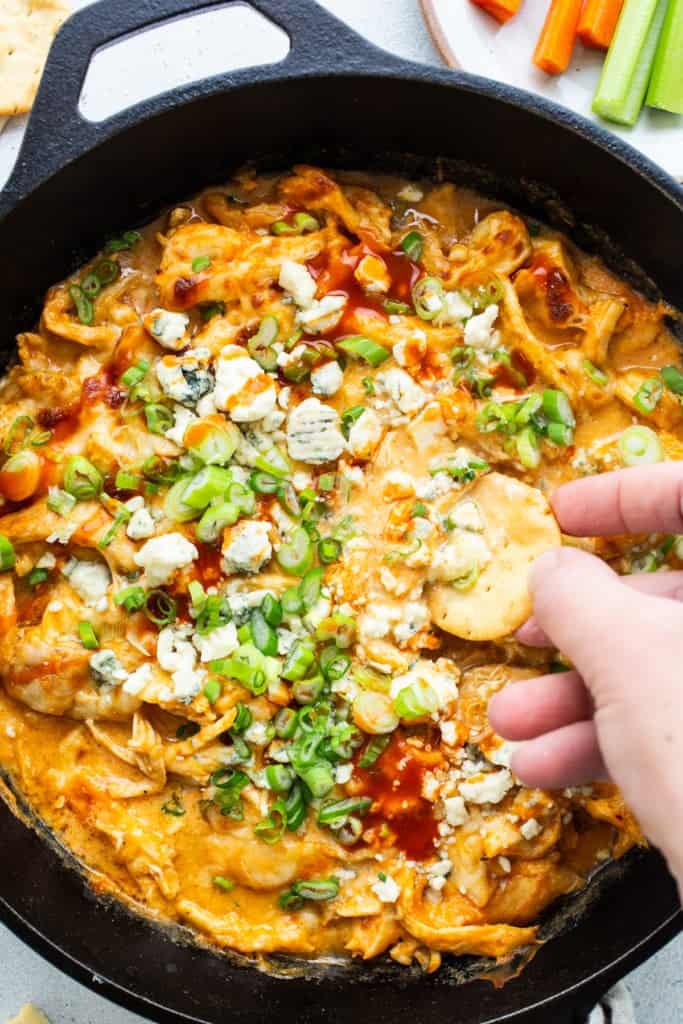 A person dipping into a skillet of buffalo chicken dip.