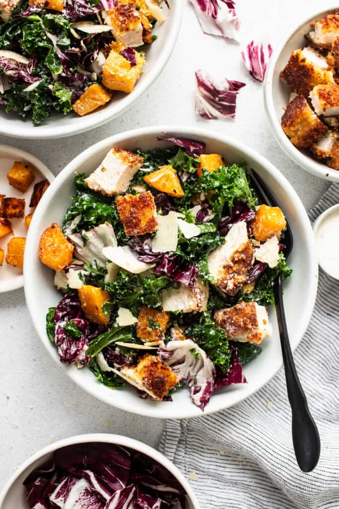 A bowl of chicken kale salad with dressing.