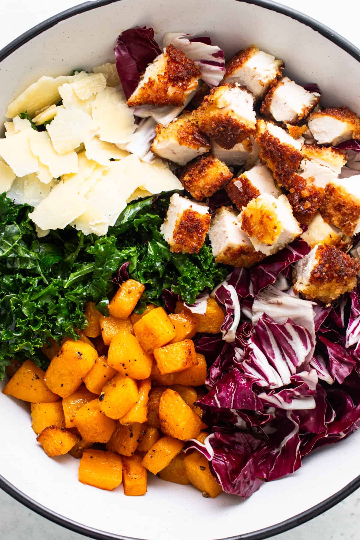 A bowl with chicken, kale, and parmesan.