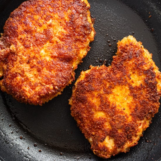 Two fried chicken patties in a frying pan.