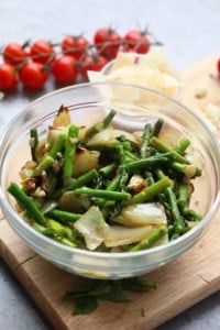 A bowl of shrimp scampi with asparagus on a cutting board.