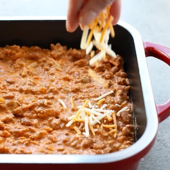 A person drizzling chili cheese dip over a casserole dish.