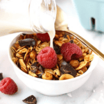 A bowl of chickpea granola with milk and raspberries.