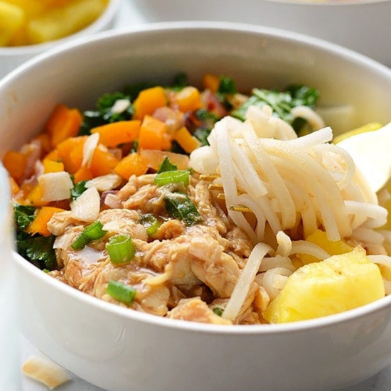 A bowl of Hawaiian chicken noodle soup with carrots and pineapples.