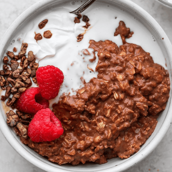 A bowl of chocolate protein oatmeal with raspberries and whipped cream.