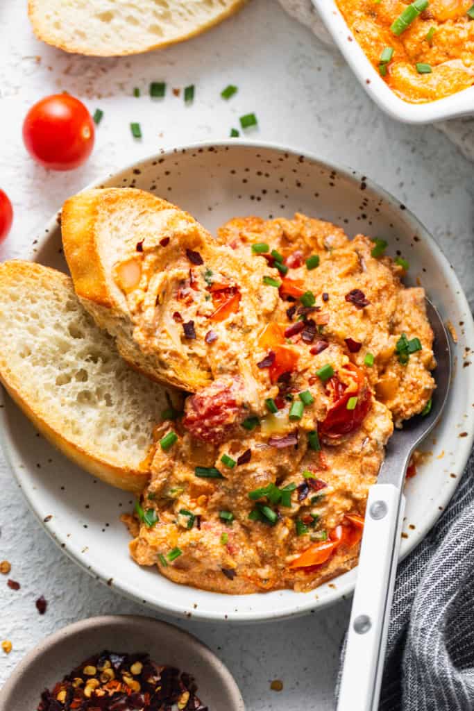 A plate of dip with bread and tomatoes.