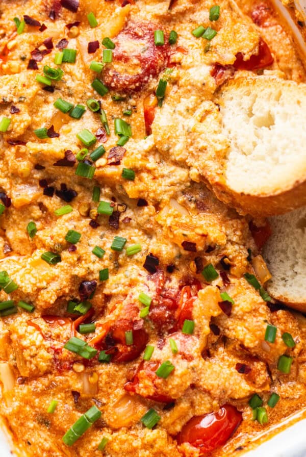 A casserole dish with chicken, tomatoes and bread.