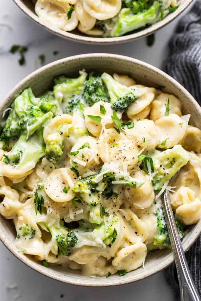 Two bowls of pasta with broccoli and parmesan cheese.