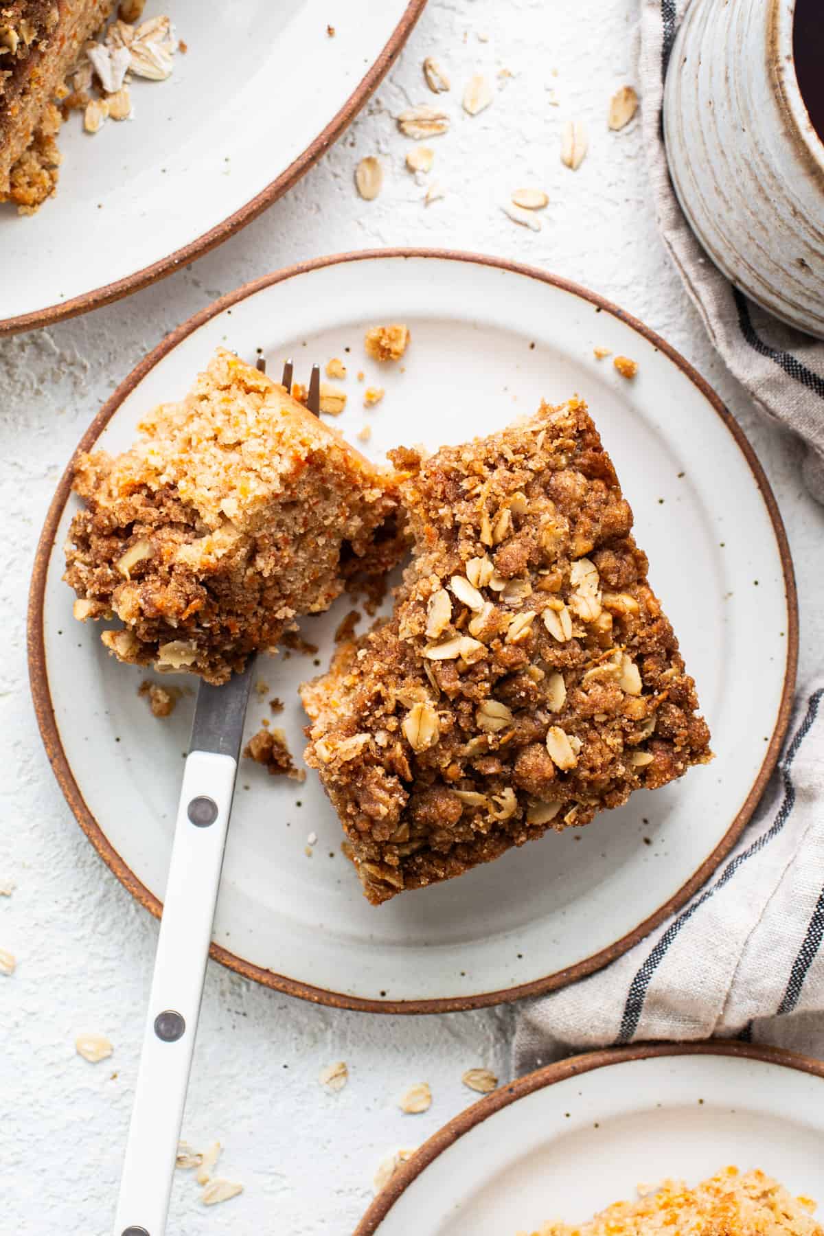 A slice of oatmeal cake on a plate next to a cup of coffee.