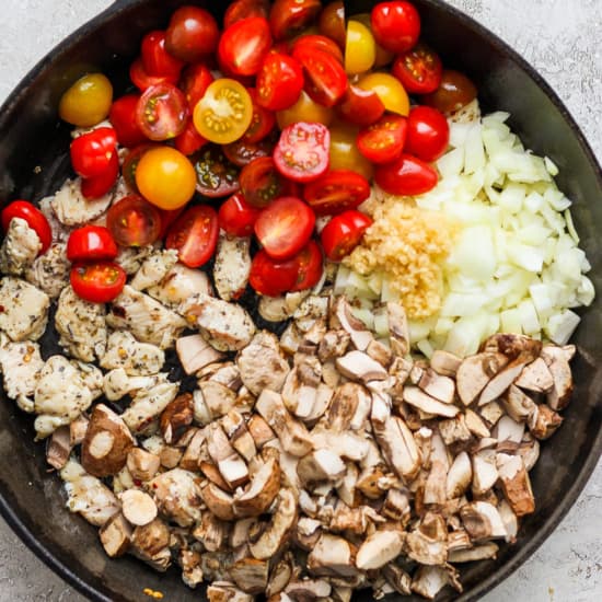 A frying pan with tomatoes, onions, and mushrooms.