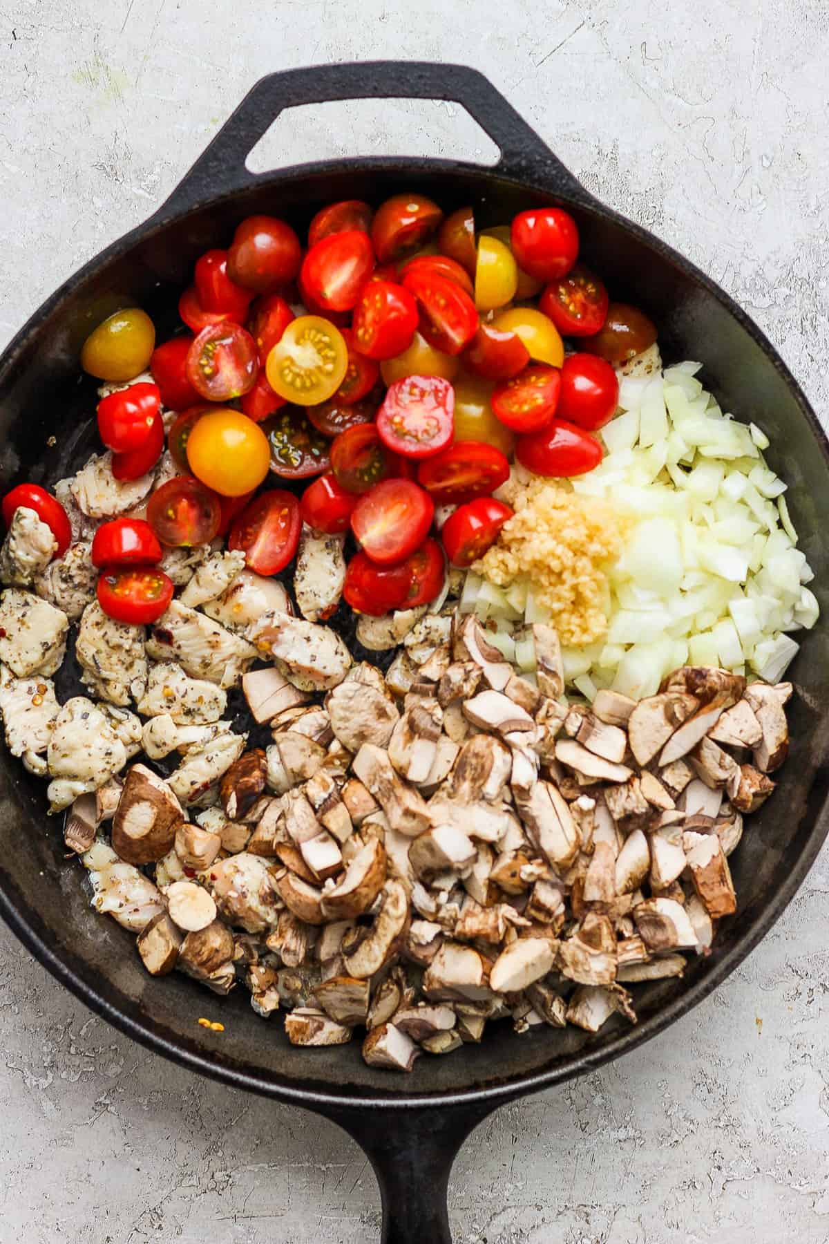 A frying pan with tomatoes, onions, and mushrooms.