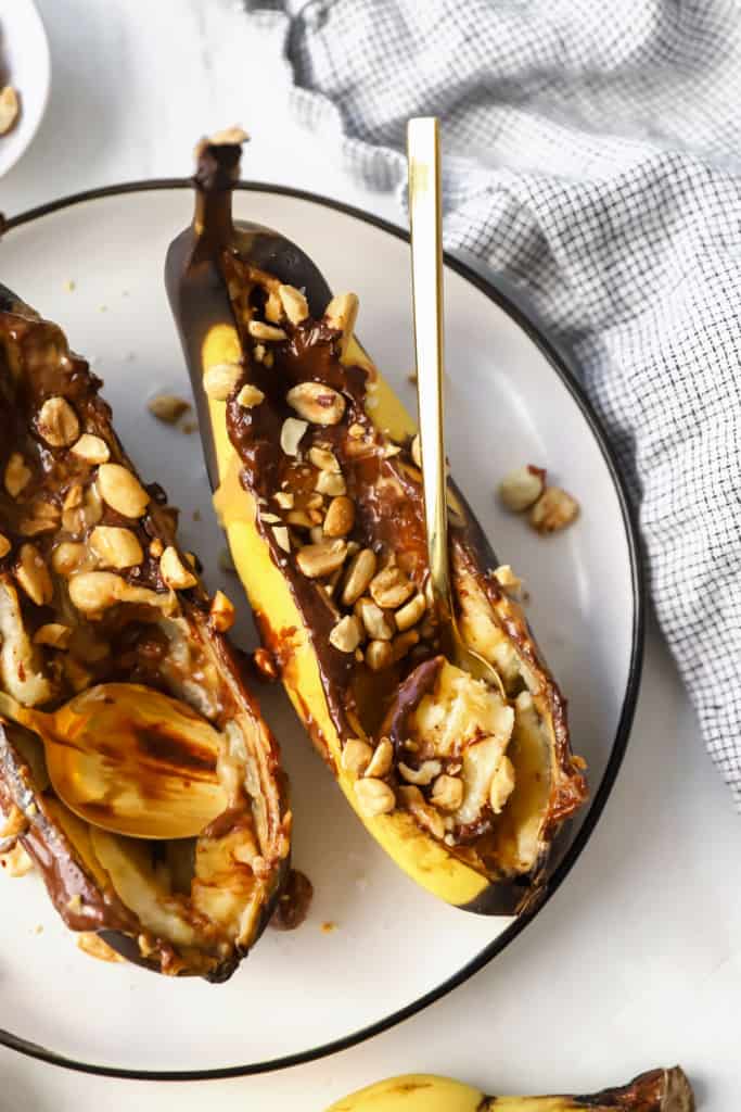 Two stuffed bananas on a plate with nuts.