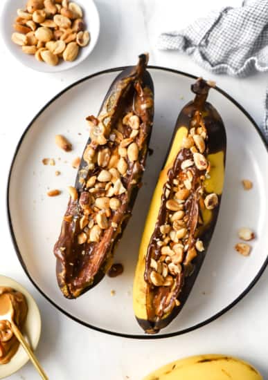 Two bananas with peanut butter and nuts on a plate.