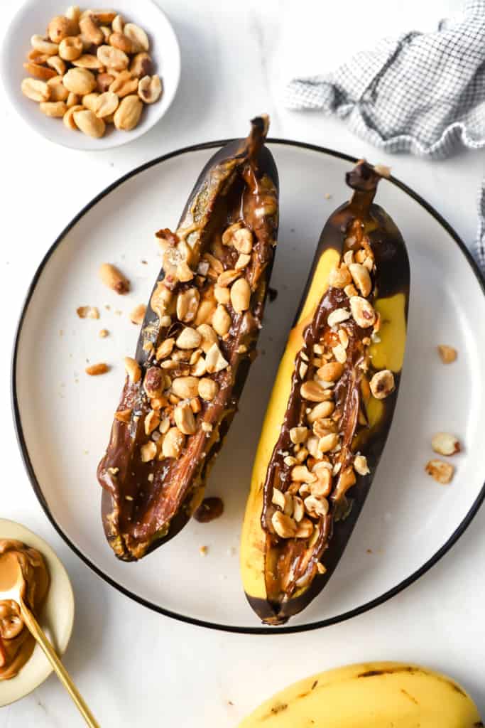Two bananas with peanut butter and nuts on a plate.