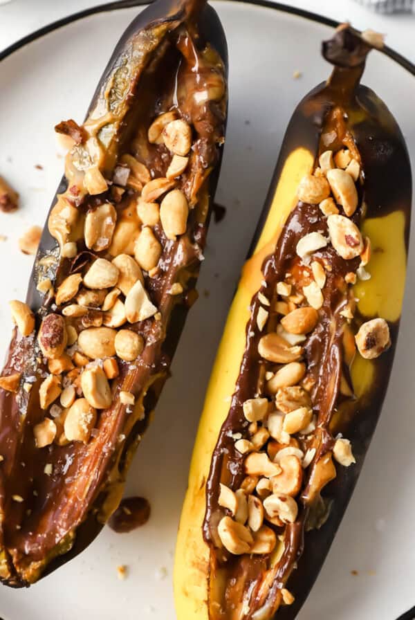 Two bananas with peanuts and chocolate on a plate.