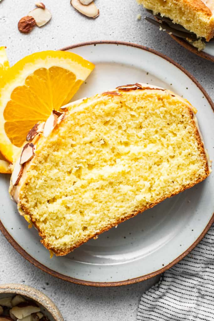 A slice of orange cake with almonds on a plate.