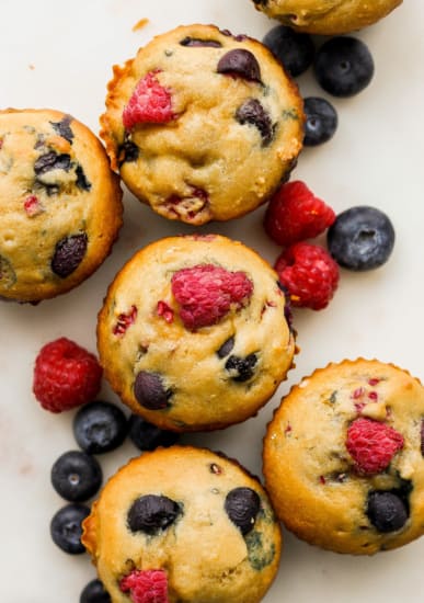 A group of muffins with raspberries and blueberries on top.