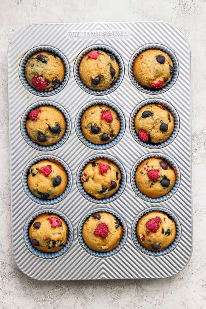 Muffins in a muffin tin with raspberries and blueberries.